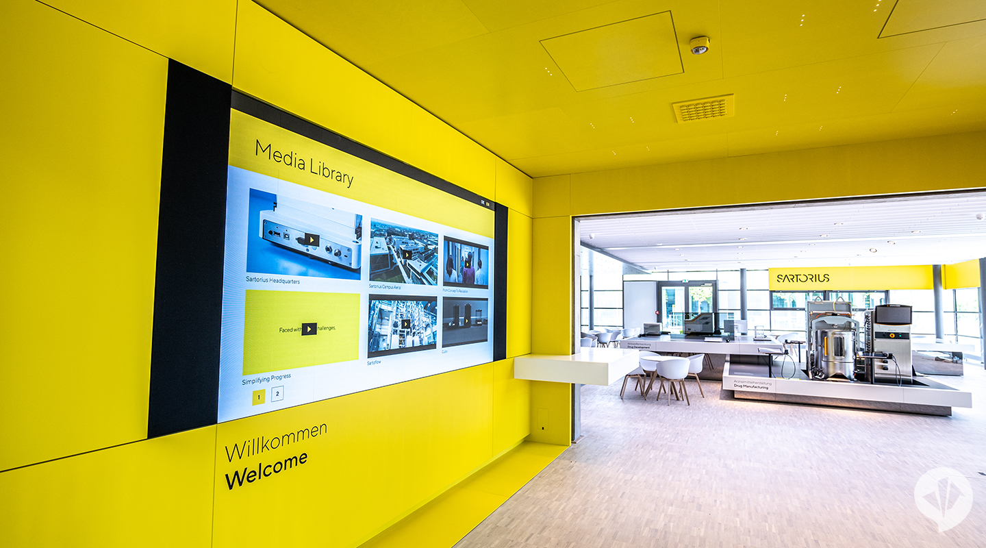 A meeting room with a yellow cinema area in the front and an open space in the back that contains displays and machine parts. The walls are made of glass.